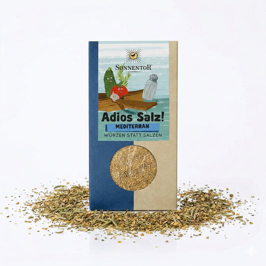 Packung Sonnentor Mediterrane Gemüsemischung Adios Salz! mit Sichtfenster, umgeben von verstreuten Bio-Gewürzen auf weißem Hintergrund.