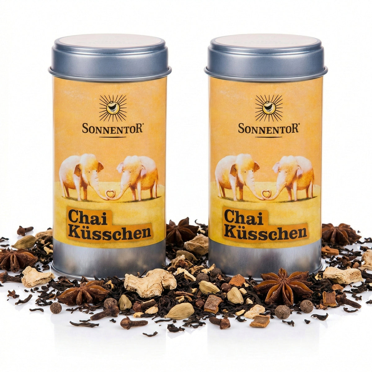 Zwei Sonnentor Chai Küsschen Gewürz-Dosen à 2x70g, umgeben von losen Gewürzen wie Sternanis, Kardamom und Ingwer auf weißem Hintergrund.