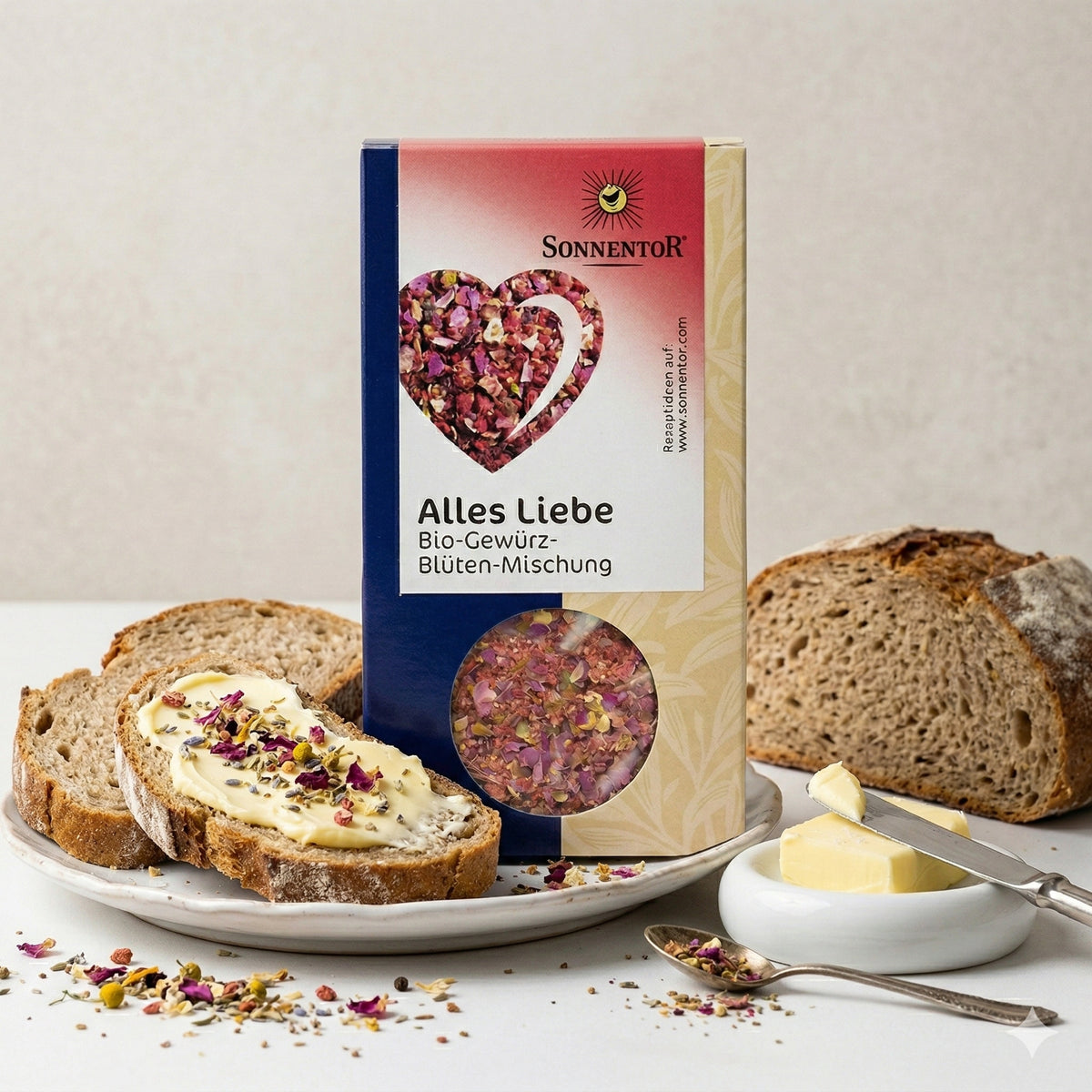 Sonnentor Alles Liebe Gewürz-Blüten-Mischung neben Brot mit Butter und Blüten-Topping, auf einem Teller mit Butterstücken und Messer.