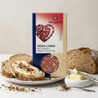 Sonnentor Alles Liebe Gewürz-Blüten-Mischung neben Brot mit Butter und Blüten-Topping, auf einem Teller mit Butterstücken und Messer.