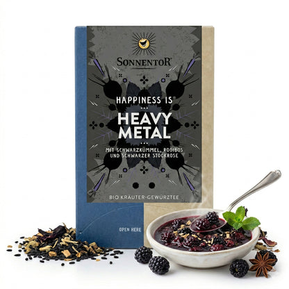 Sonnentor Heavy Metal Tee-Packung neben einer Schale mit Beerenkompott, Minze, Sternanis und losen Kräutertee-Zutaten.