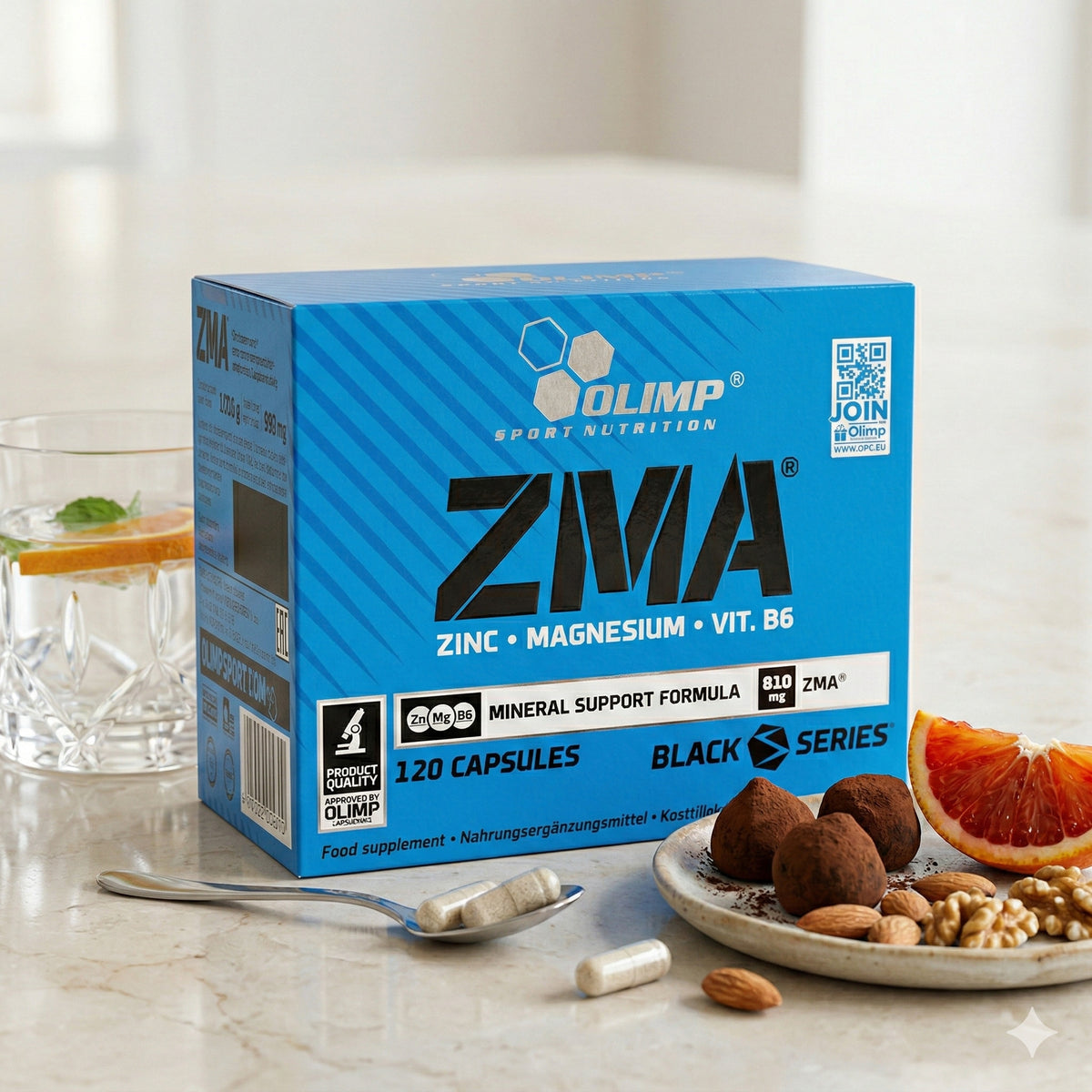 Olimp ZMA Packung mit Kapseln auf einem Löffel, daneben ein Glas Wasser, Nüsse, Trüffel und eine Blutorangenscheibe auf einem Teller, alles auf einem hellen Tisch.