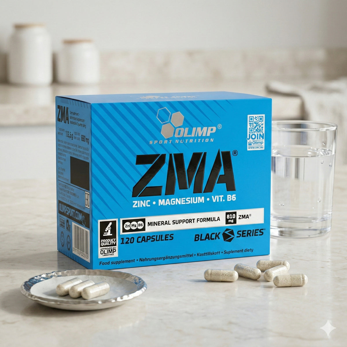 Olimp ZMA Caps Packung auf einer Küchenarbeitsplatte, daneben ein Glas Wasser und mehrere Kapseln auf einem kleinen Teller sowie lose auf dem Tisch verteilt.