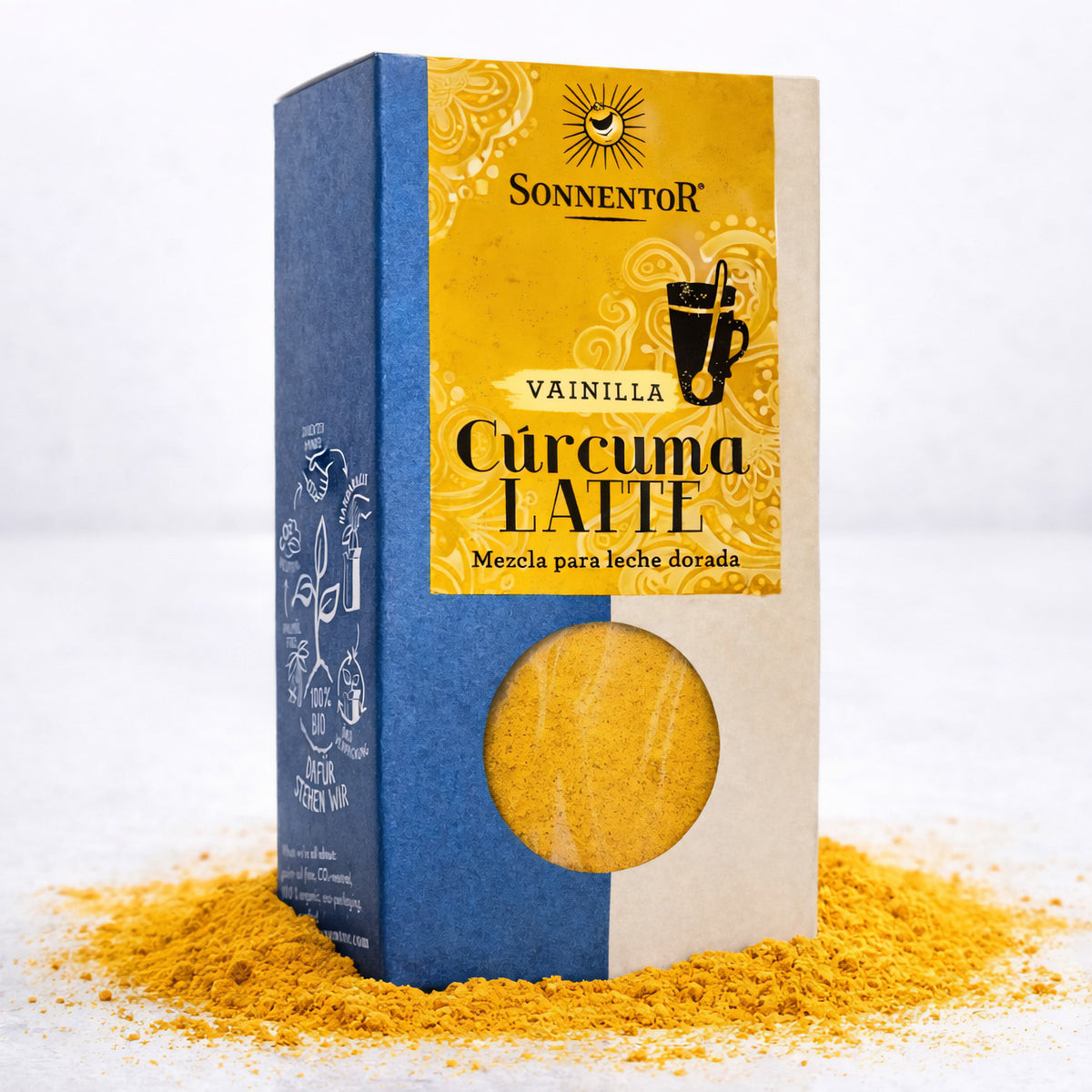 Packung Sonnentor Gewürzmischung Kurkuma Latte Vanilla, 3x60g, stehend auf verstreutem gelbem Kurkuma-Pulver, Vorderseite mit Sichtfenster und Etikett sichtbar.