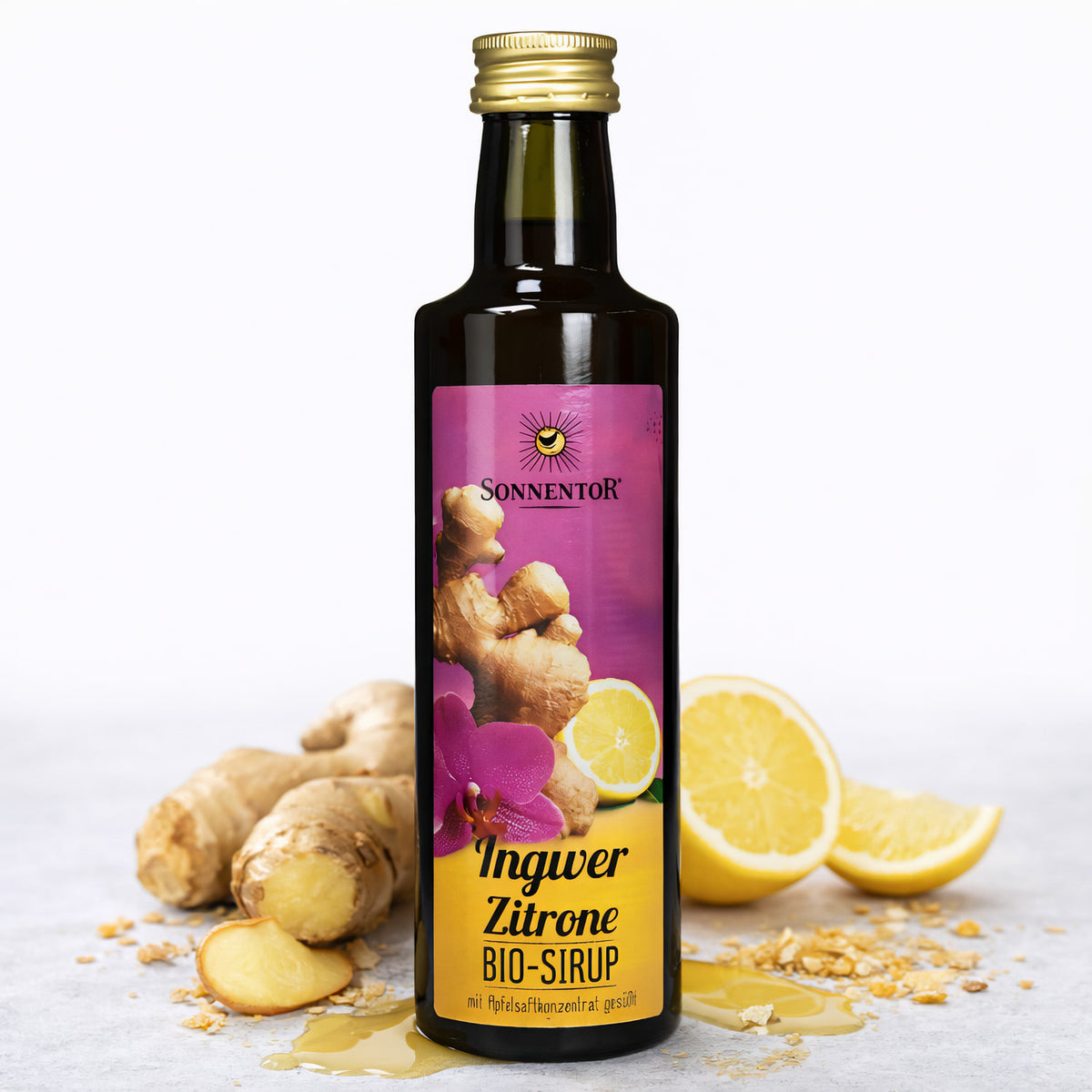 Sonnentor Ingwer-Zitronen Sirup in dunkler Flasche, davor frischer Ingwer, Zitronenscheiben und etwas ausgelaufener Sirup auf hellem Untergrund.