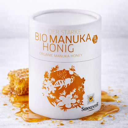 Sonnentor starke Manukahonig 250g in weißer Dose, daneben Honigwabe und ausgelaufener Honig als Aufstrich.
