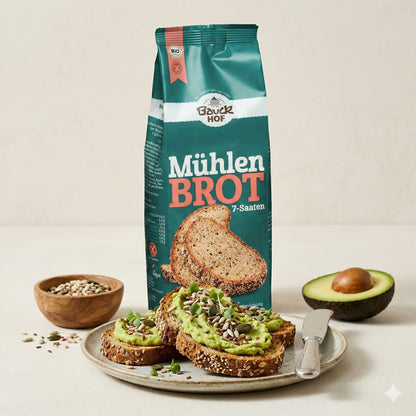 Bauckhof Mühlenbrot 7-Saaten Backmischung neben belegten Brotscheiben mit Avocado und Saaten, Avocadohälfte und Schale mit Saaten im Hintergrund.