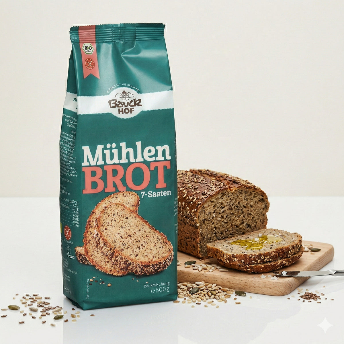Bauckhof Mühlenbrot 7-Saaten Backmischung vor angeschnittenem Saatenbrot auf Holzbrett, Brotscheibe mit Öl bestrichen.