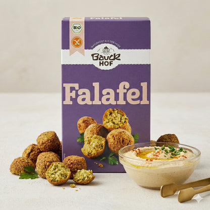 Bauckhof Falafel Mischung glutenfrei mit angerichteten Falafel-Bällchen und einer Schale Hummus mit Kräutern und zwei goldenen Löffeln.