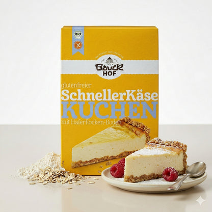 Packung Bauckhof schnelle Käsekuchen Backmischung glutenfrei 485g, davor ein Stück Käsekuchen auf Teller mit Himbeeren und zwei Löffeln.