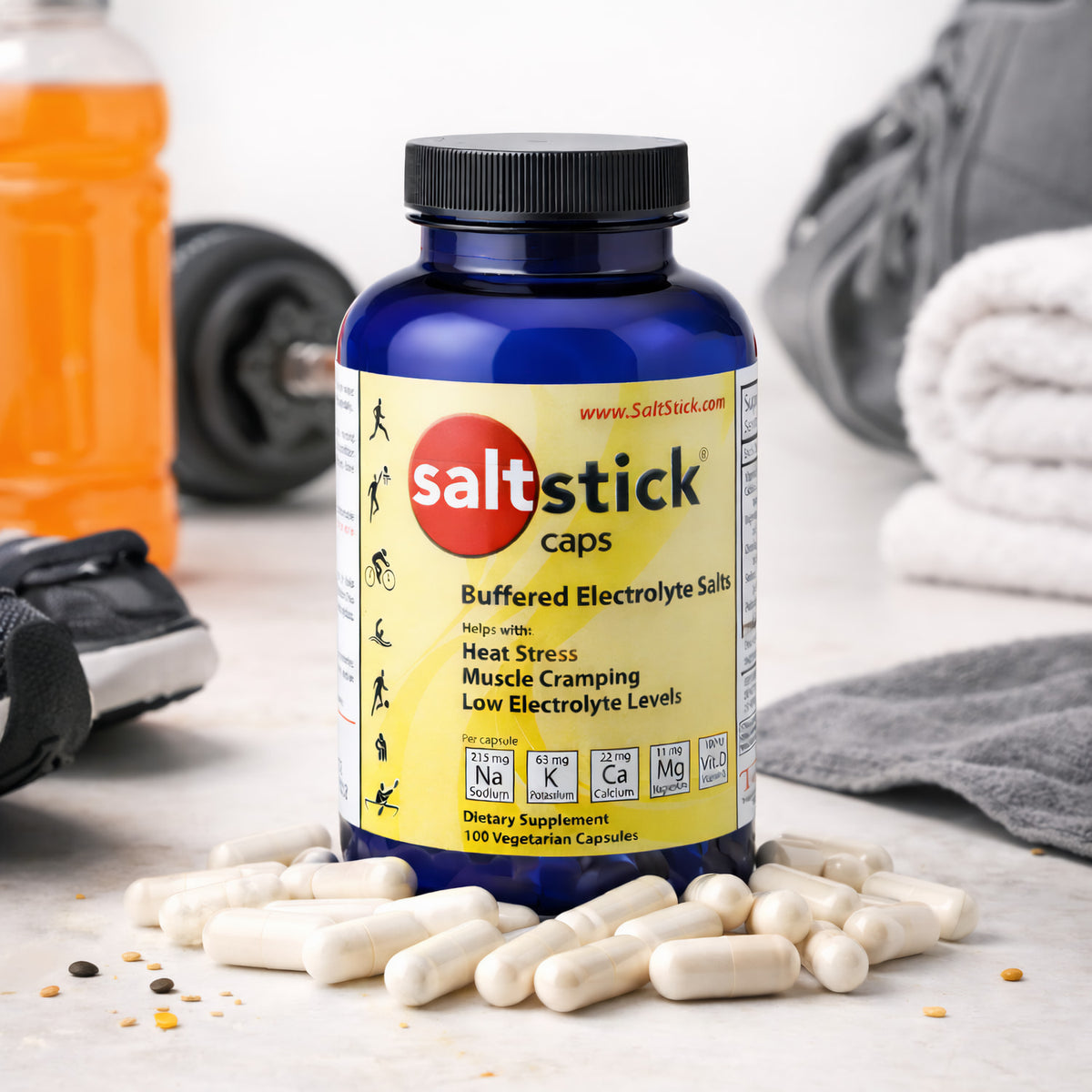 SaltStick Elektrolyte-Kapseln vor blauer Dose, im Hintergrund Sportausrüstung wie Hantel, Sportschuh, Handtuch und Getränk.