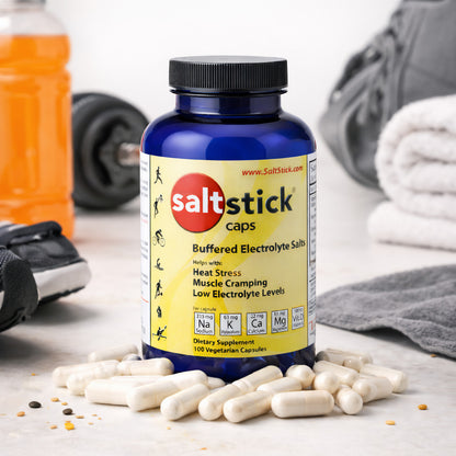 SaltStick Elektrolyte-Kapseln vor blauer Dose, im Hintergrund Sportausrüstung wie Hantel, Sportschuh, Handtuch und Getränk.