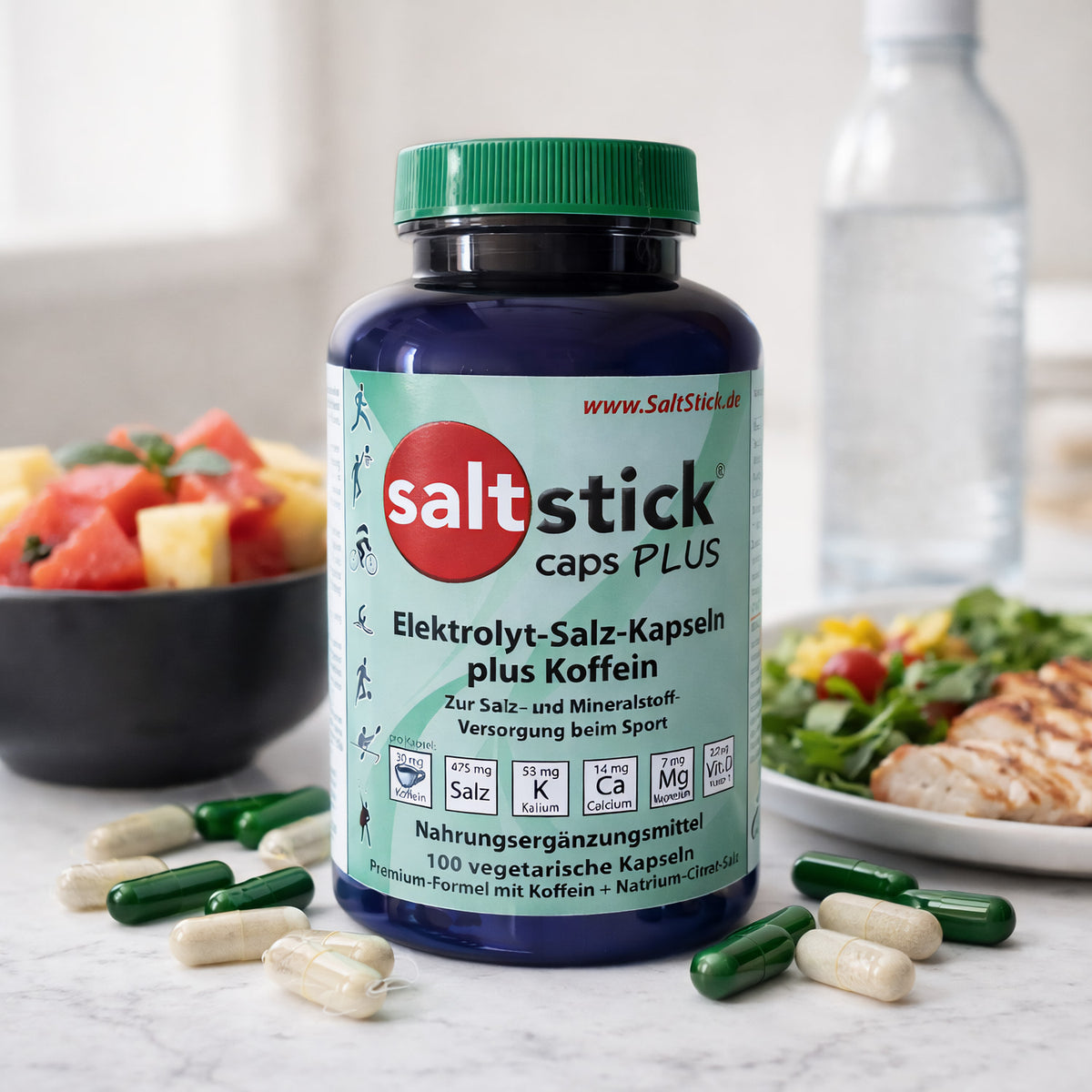 SaltStick Caps Plus Dose mit Kapseln im Vordergrund, im Hintergrund eine Schale Obst, ein Teller mit Salat und Hähnchen sowie eine Wasserflasche, Fokus auf elektrolyt kapseln.