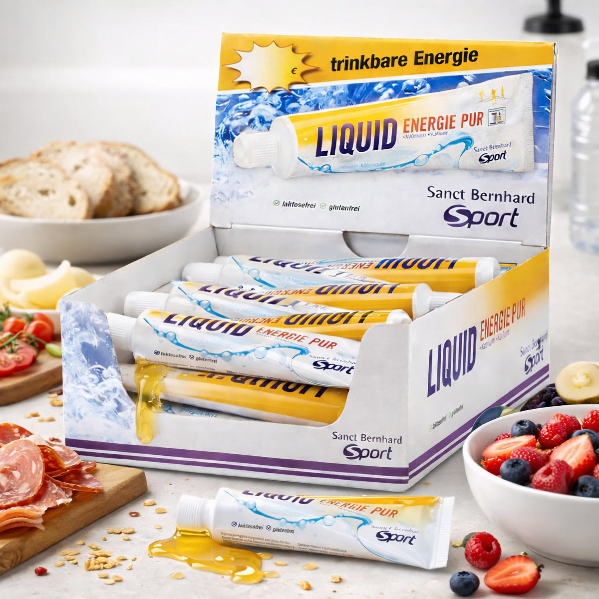 aktiv3 liquid energie Tuben von sanct bernhard sport in offener Verpackung, vorne ausgelaufene Tube, daneben Schale mit Obst und Teller mit Brot und Wurst.