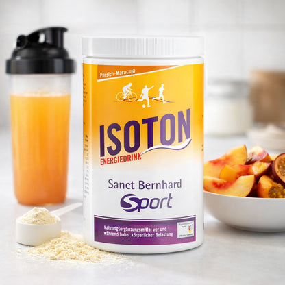 Sanct Bernhard SPORT Isoton Energiedrink 900g Dose mit Messlöffel Pulver, Shaker mit zubereitetem Energiedrink und Schale mit Pfirsich- und Maracuja-Stücken im Hintergrund.