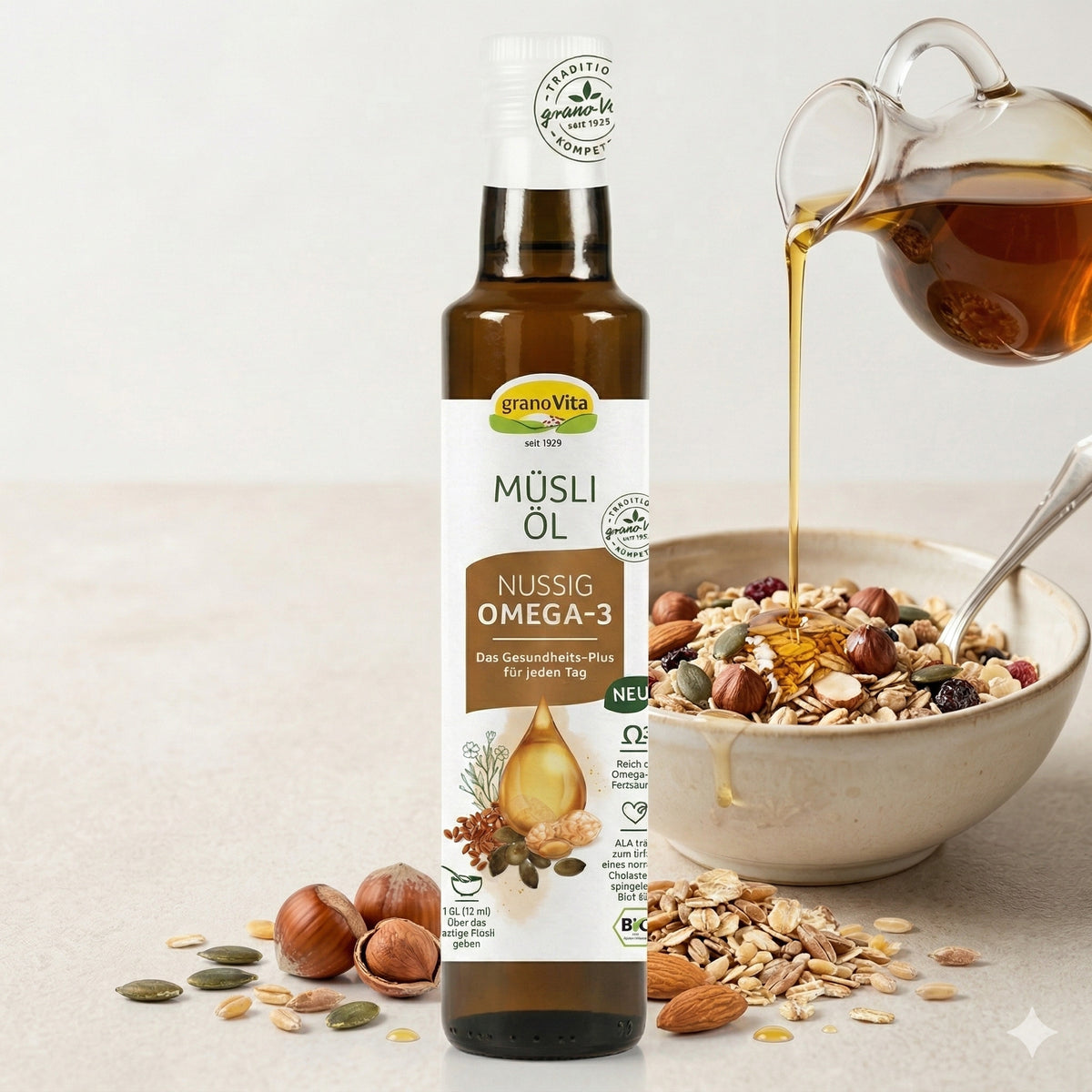 Müsliöl von Grano Vita nussig vor einer Müslibowl, in die gerade Öl aus einer Kanne als Topping gegossen wird, daneben Müslizutaten.