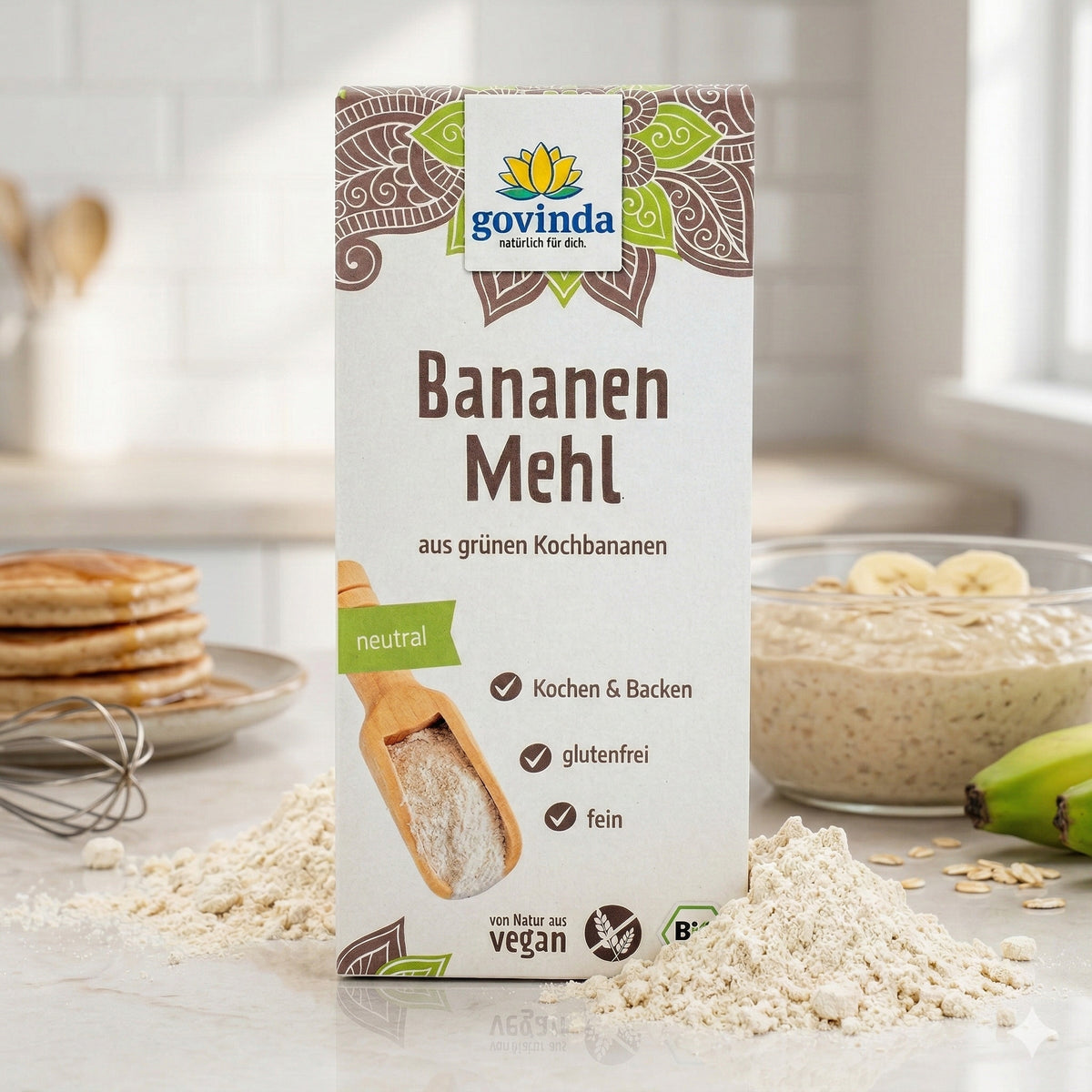 Govinda Bananenmehl aus grünen Kochbananen, 350g, in Küche mit Mehlhaufen, Pancakes, Schneebesen und Bananenbrei im Hintergrund