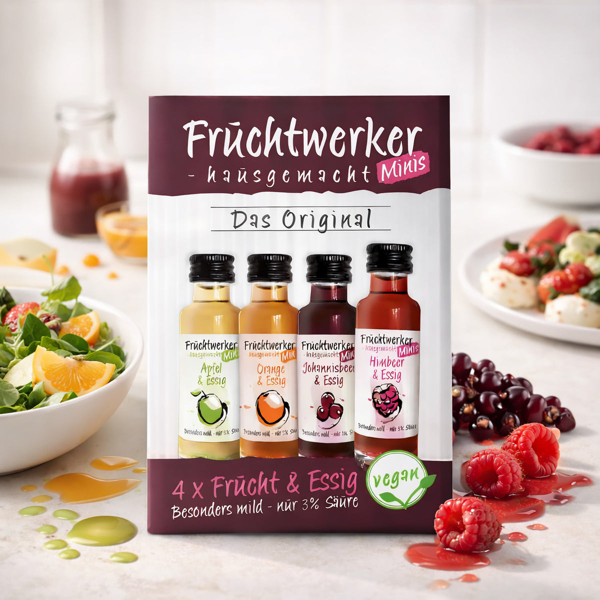 Fruchtwerker Minis 4er-Set vor einer Küche mit Salat und Mozzarella, die Fläschchen Apfel, Orange, Johannisbeere und Himbeere stehen im Vordergrund.