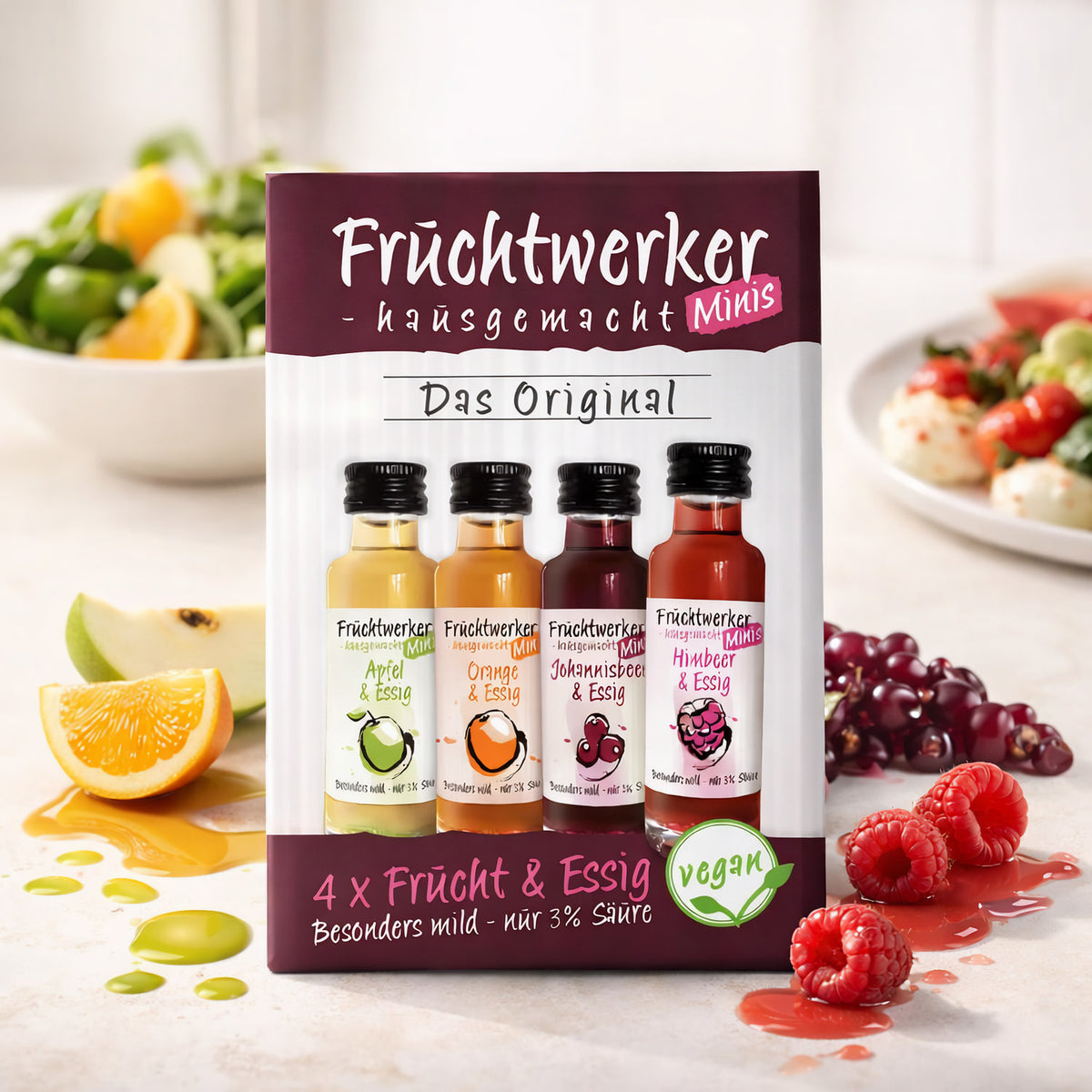 Fruchtwerker Minis 4er-Set mit Essigsorten Apfel, Orange, Johannisbeere und Himbeere, im Küchenumfeld mit Salat und fruchtigen Zutaten dekoriert.