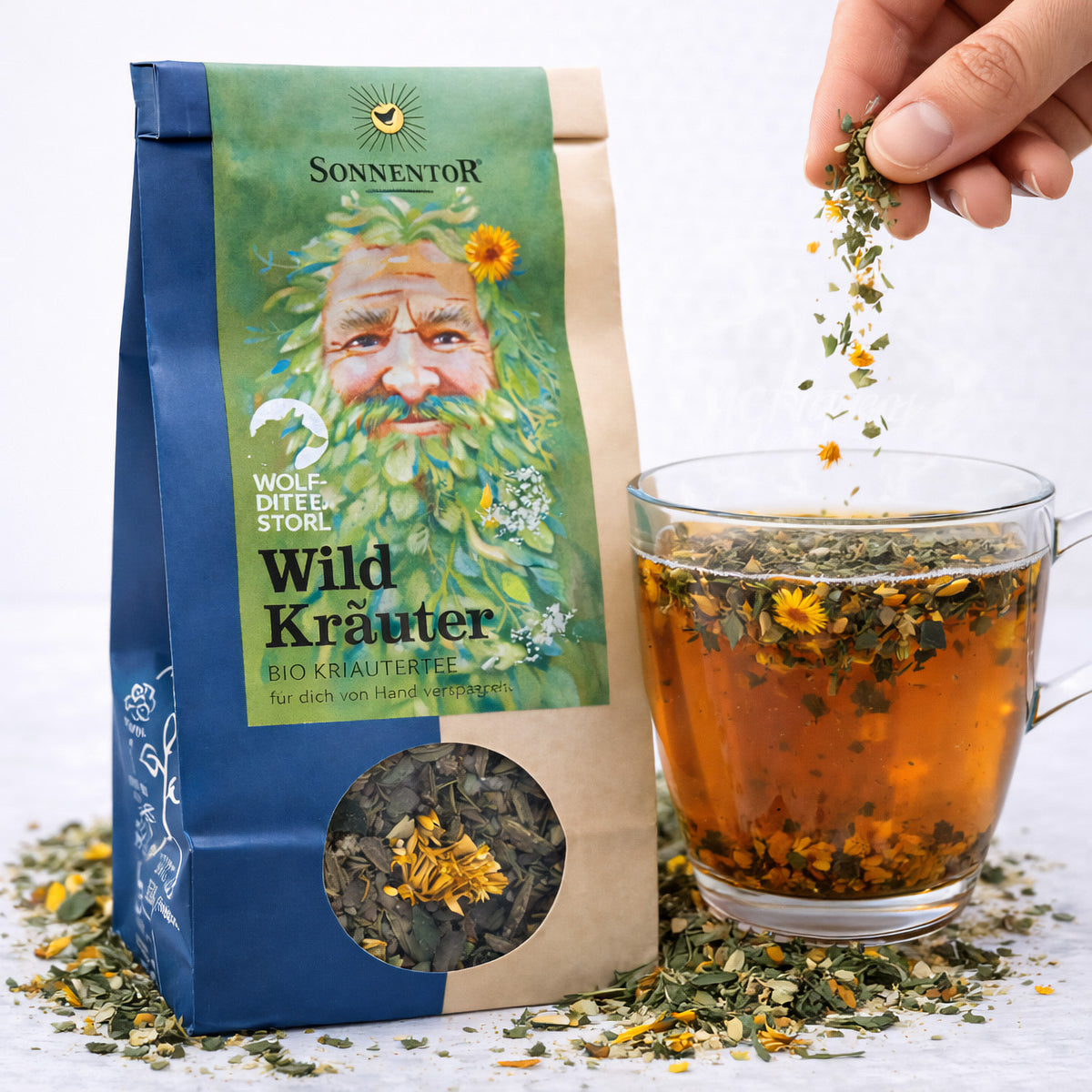 Bio Wildkräuter-Tee von Sonnentor in einer Packung, frische Kräuter für aromatischen Genuss, geöffnete Teetasse mit Kräutern.