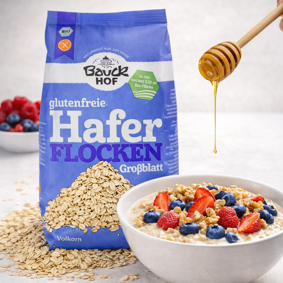 Bauckhof Haferflocken Grob 475g neben einer Schale Porridge mit Beeren und Honig, im Hintergrund frische Früchte.