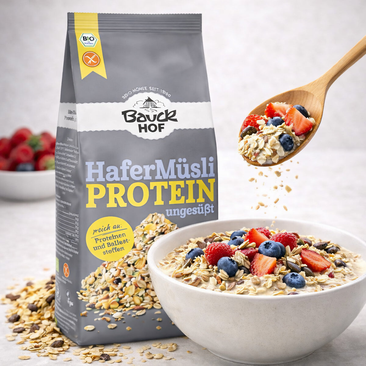 Bauckhof Hafer Müsli Protein glutenfrei in Schale mit Milch und frischen Beeren, daneben die geöffnete Packung und ein Holzlöffel.