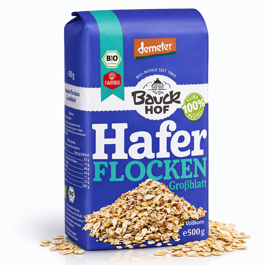 Packung Bauckhof Bio Haferflocken Großblatt Demeter 500g stehend, vorne sichtbar, mit lose verstreuten Haferflocken davor auf weißem Hintergrund.