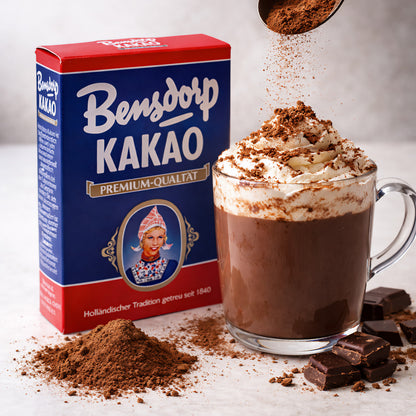 Bensdorp Kakao Getränkepulver neben einer Tasse Trinkschokolade mit Sahne, Kakaopulver und Schokoladenstücken.