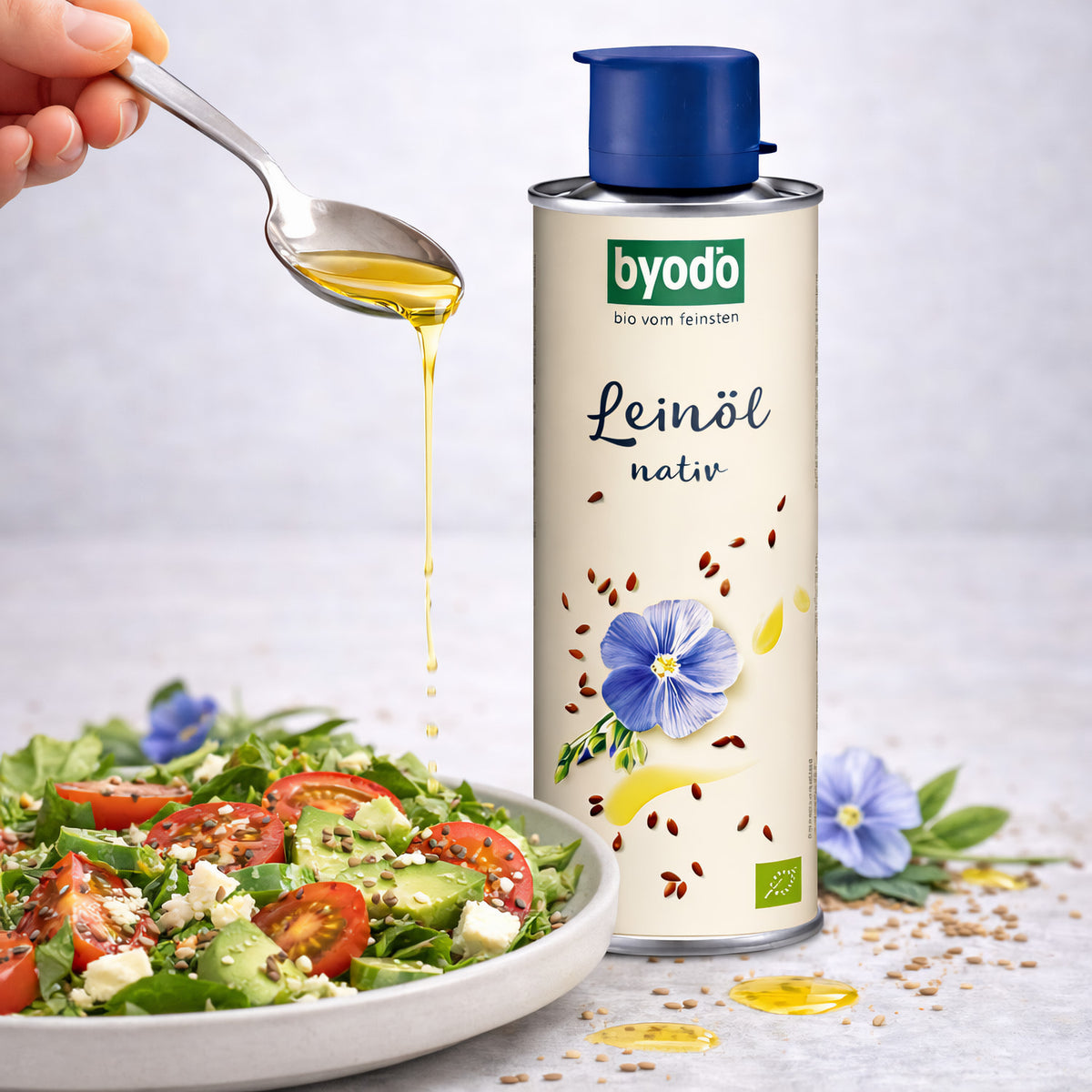 byodo leinöl nativ in der dose neben einem frischen Salat, Öl wird mit einem Löffel über den Salat geträufelt