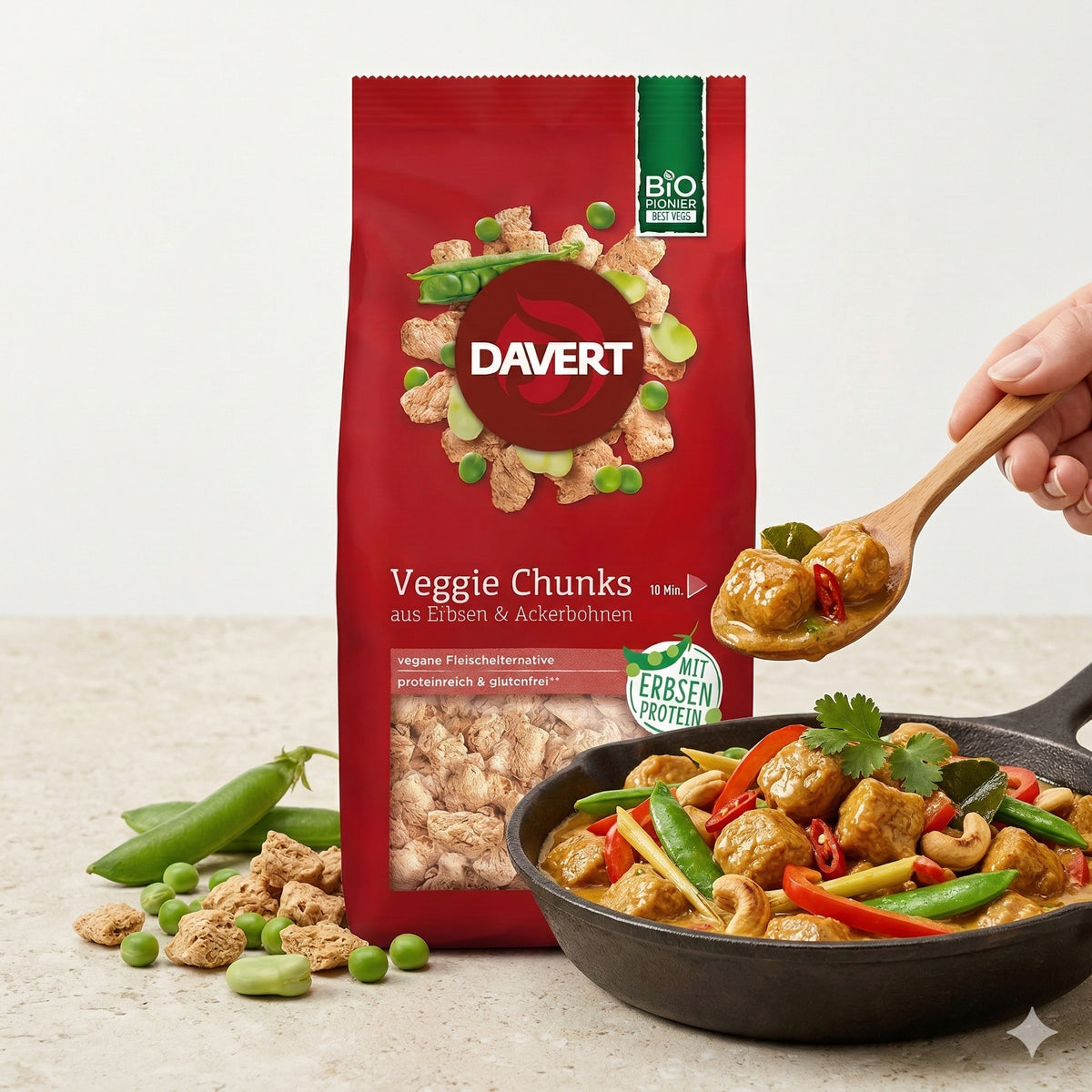 Davert Veggie Chunks 100g vor einer Pfanne mit Currygericht, Gemüse und Chunks, eine Hand serviert mit einem Holzlöffel.