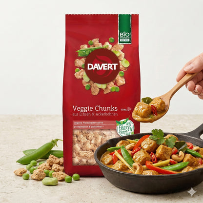 Davert Veggie Chunks 100g vor einer Pfanne mit Currygericht, Gemüse und Chunks, eine Hand serviert mit einem Holzlöffel.