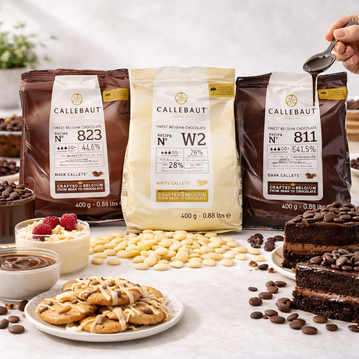 Callebaut Kuvertüre Callets 3x400g mit Zartbitter-, Milch- und weißer Schokolade, umgeben von Cookies, Kuchen, Schoko-Callets und einer Hand, die Schokolade über Kuchen gießt.