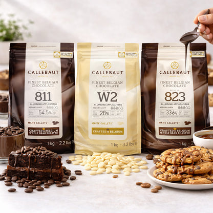 Callebaut Kuvertüre Callets Zartbitter-, Milch- und weiße Schokolade, 3x1000g, stehend zwischen Schokoladenkuchen, Keksen und Schokoladentropfen, im Hintergrund Backzutaten.