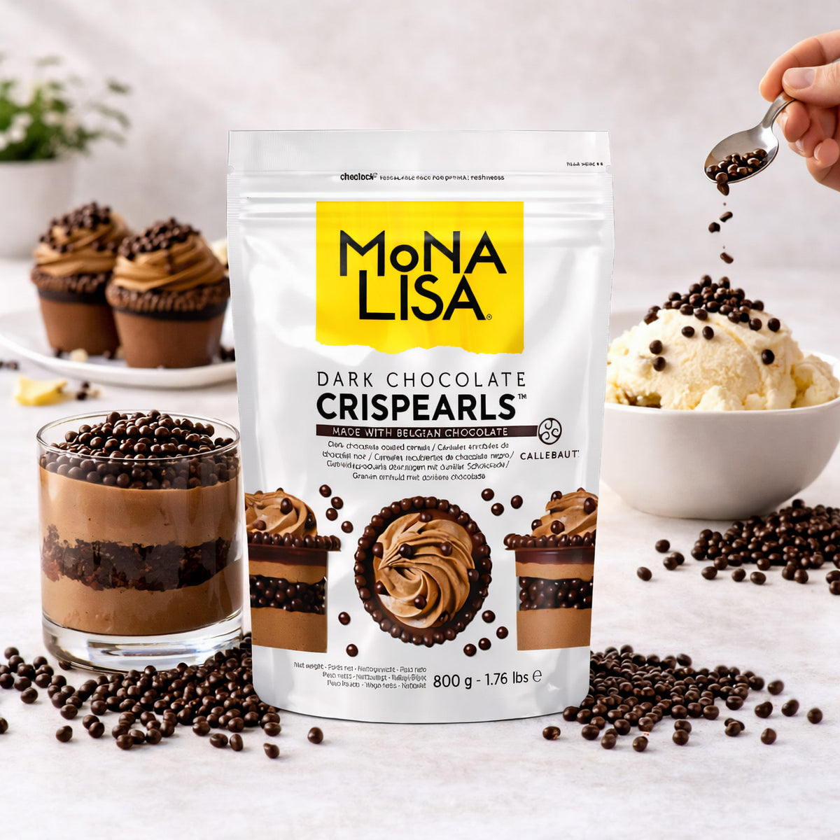 Callebaut Crispearls dark 800g vor Dessert und Eis, Schokoladenperlen werden mit einem Löffel auf Eis gestreut, weitere Backwaren im Hintergrund.