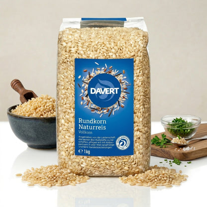 Davert Natur Rundkornreis 1 kg, stehend, im Vordergrund Reis, im Hintergrund Schale mit Reis und Kräuter auf Glasplatte.