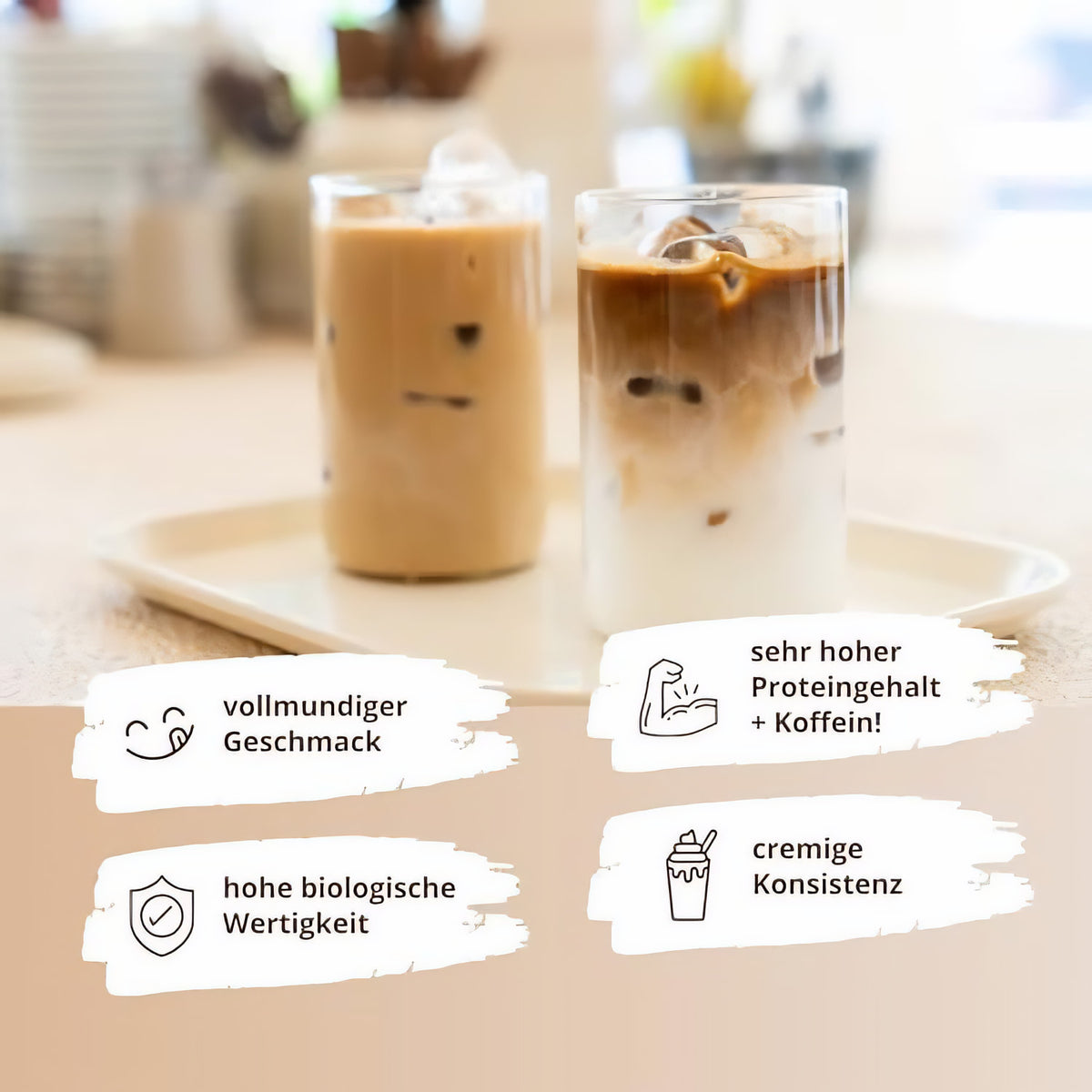 Zwei Gläser mit eisgekühltem proteinkaffee auf einem Tablett, links helles, rechts geschichtetes Kaffeegetränk, im Hintergrund verschwommene Küche.