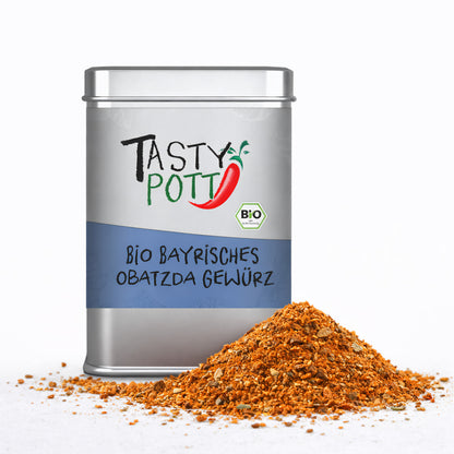 Tasty Pott Bio Bayrisches Obatzda Gewürz in silberner Dose mit blauem Etikett, davor ein Haufen der orangen Gewürzmischung auf weißem Untergrund.