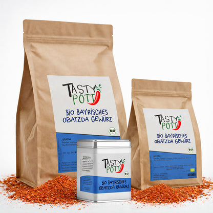 Drei Tasty Pott Nachfüllbeutel und eine Gewürzdose Bio Bayrisches Obatzda Gewürz in verschiedenen Größen, stehend auf verstreutem Gewürzpulver.