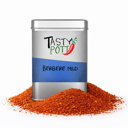 Tasty Pott Berbere mild äthiopische Gewürzmischung in silberner Dose, umgeben von einem Haufen rot-oranger Gewürze.