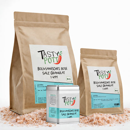 Drei Tasty Pott Nachfüllbeutel und eine Dose bolivianisches Rosé Salz Granulat auf rosa Salz liegend, Vorderseiten mit Etiketten sichtbar.