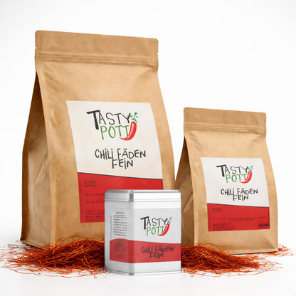 Drei Tasty Pott Nachfüllbeutel und eine Dose mit Chili Fäden fein, umgeben von losen Chilifäden auf weißem Hintergrund.