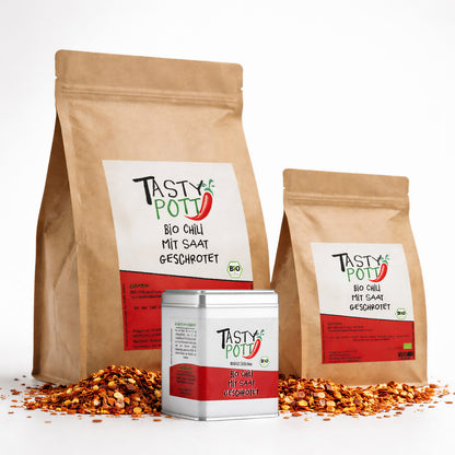 Drei Tasty Pott Beutel und eine Dose Bio Chili geschrotet mit Saat, umgeben von verstreutem Chili, als Einzelgewürze auf weißem Hintergrund.