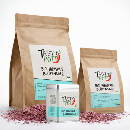 Drei Tasty Pott Hibiskusblütensalz Nachfüllbeutel und eine Dose, umgeben von rosafarbenem Hibiskussalz auf weißem Untergrund.