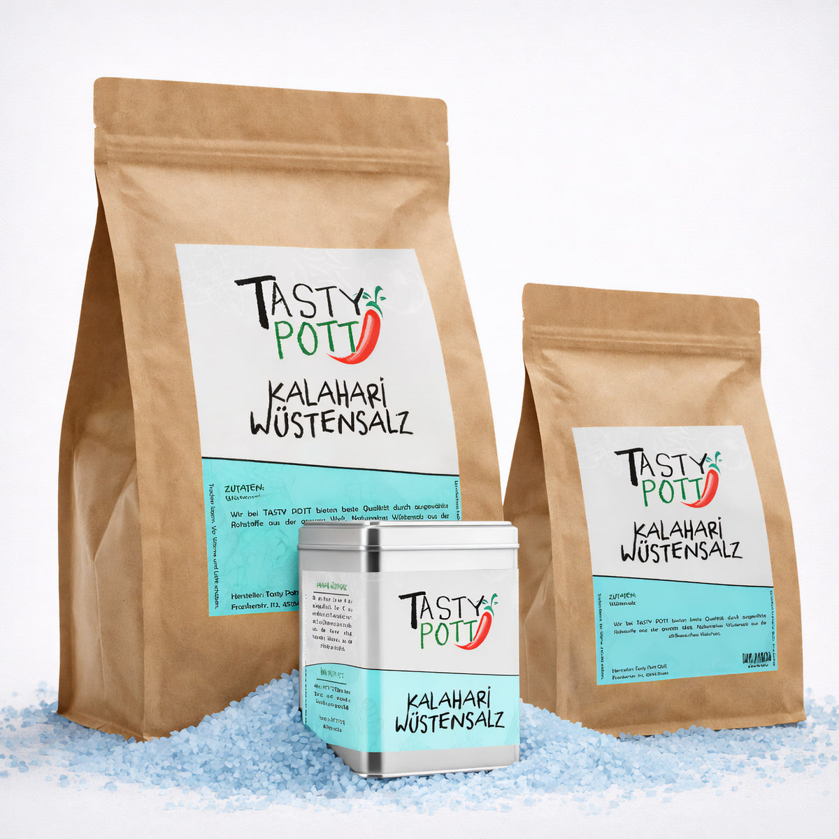 Drei Tasty Pott Kalahari Wüstensalz Verpackungen, zwei braune Nachfüllbeutel und eine silberne Dose, auf grobem blauen Salz stehend.