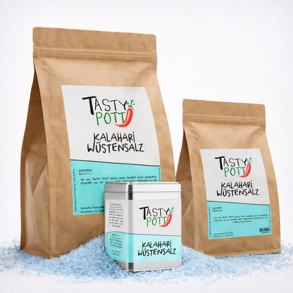 Drei Tasty Pott Kalahari Wüstensalz Verpackungen, zwei braune Nachfüllbeutel und eine silberne Dose, auf grobem blauen Salz stehend.