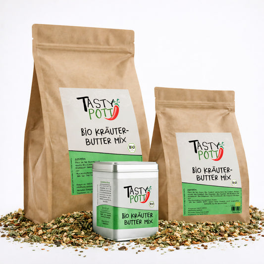 Tasty Pott Bio Kräuterbutter Gewürzmischung im braunen Nachfüllbeutel und in einer Dose, stehend auf einer Mischung aus getrockneten Kräutern und Gewürzen.