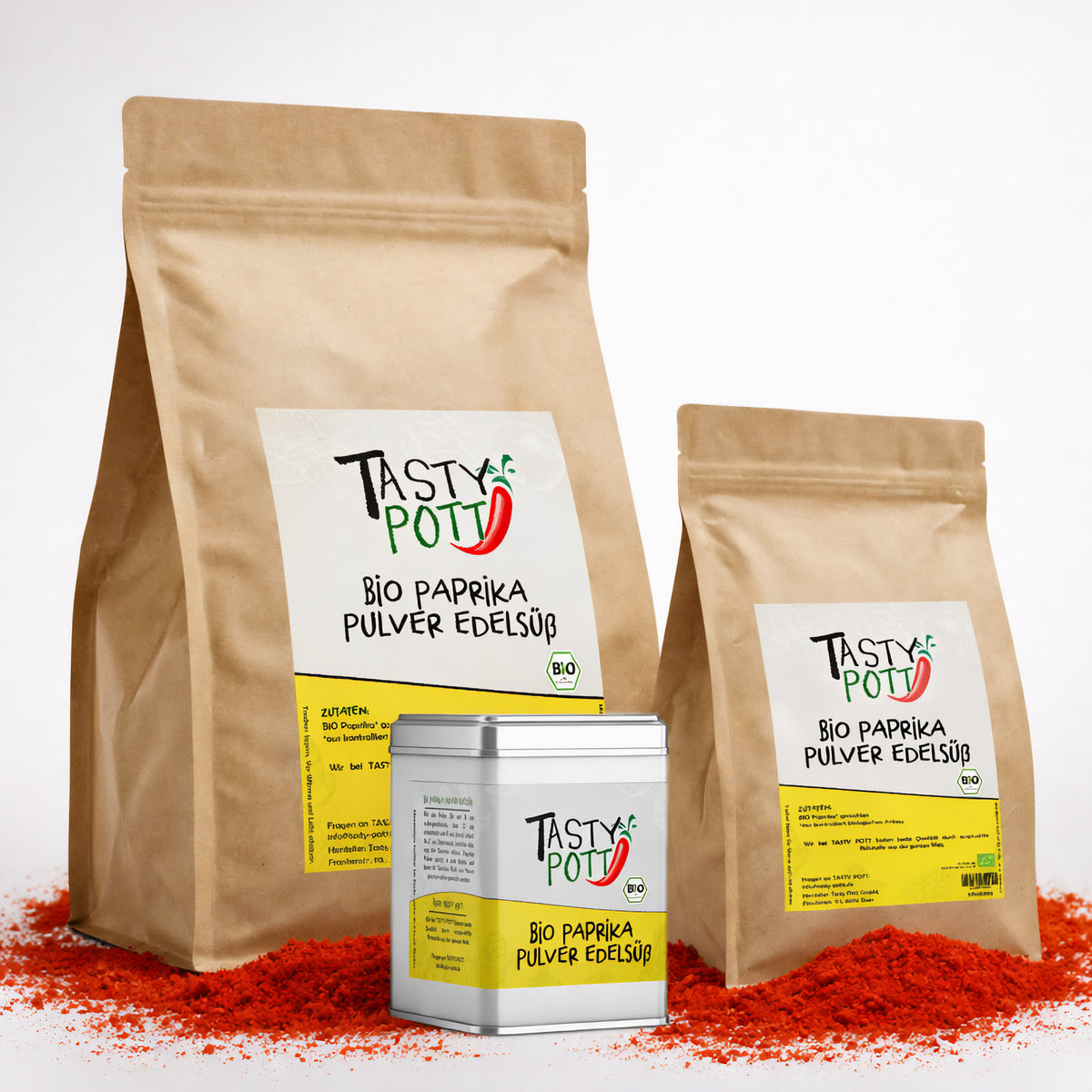 Drei Tasty Pott Bio Paprikapulver edelsüß Verpackungen im Beutel und in der Dose, stehend auf verstreutem roten Paprikapulver.