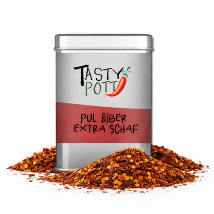 Tasty Pott Pul Biber extra scharf Dose, umgeben von Haufen grober Chili-Gewürzmischung auf weißem Hintergrund.