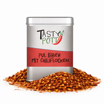 Tasty Pott Pul Biber mit Chiliflocken in silberner Dose, umgeben von einem Haufen roter Chiliflocken.