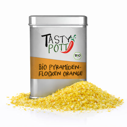 Dose Tasty Pott Bio Pyramidenflocken Orange & Salz mit pyramidenförmigen orangenen Salzflocken im Vordergrund auf weißem Hintergrund.